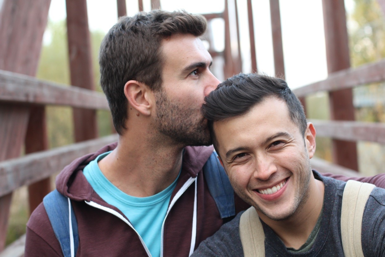 Man kissing another man's head on a bridge