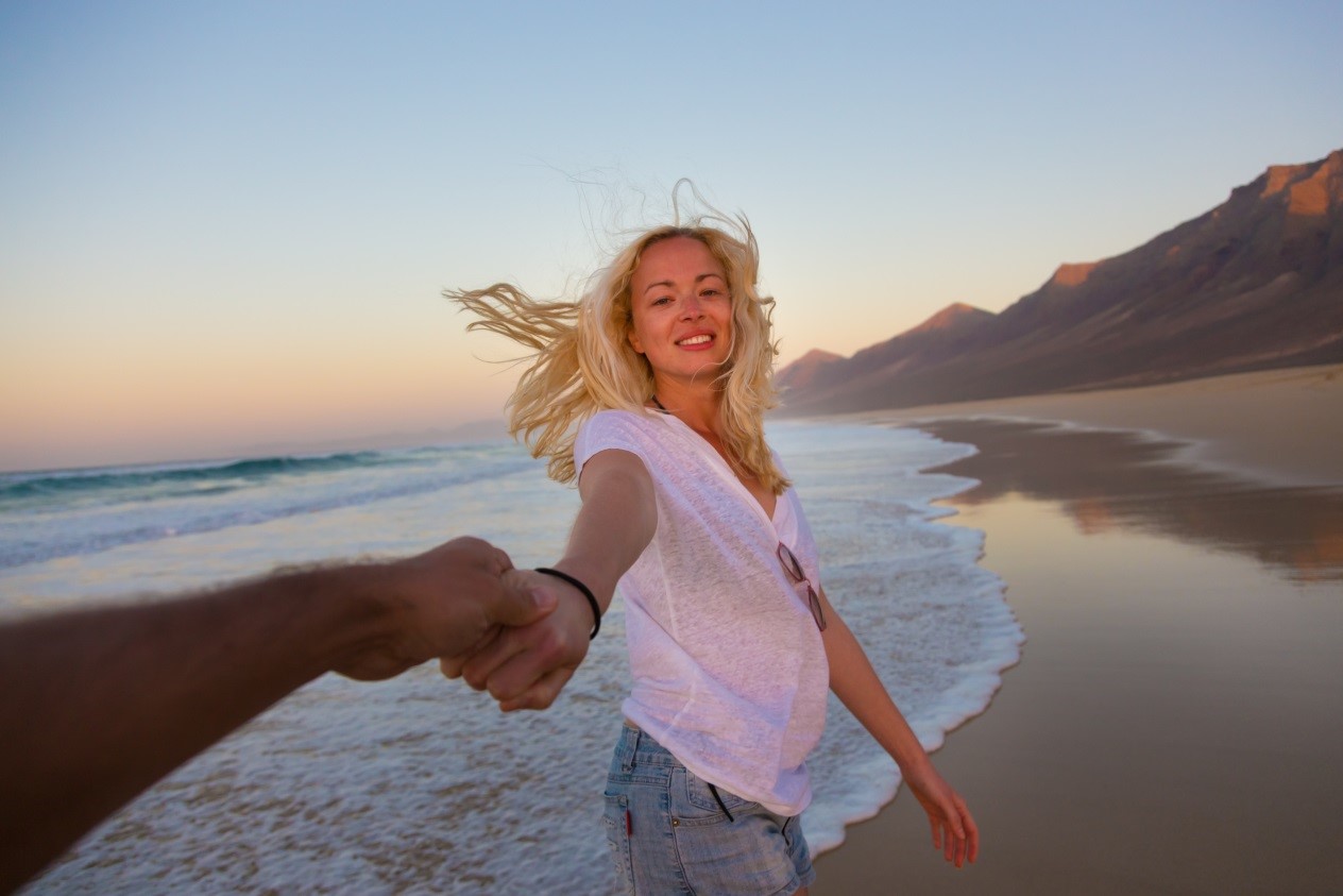 pregnant woman holding a mans hand on the beach