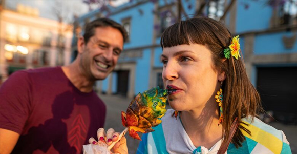 man smiling and looking a a woman trying fruta con chile y limon