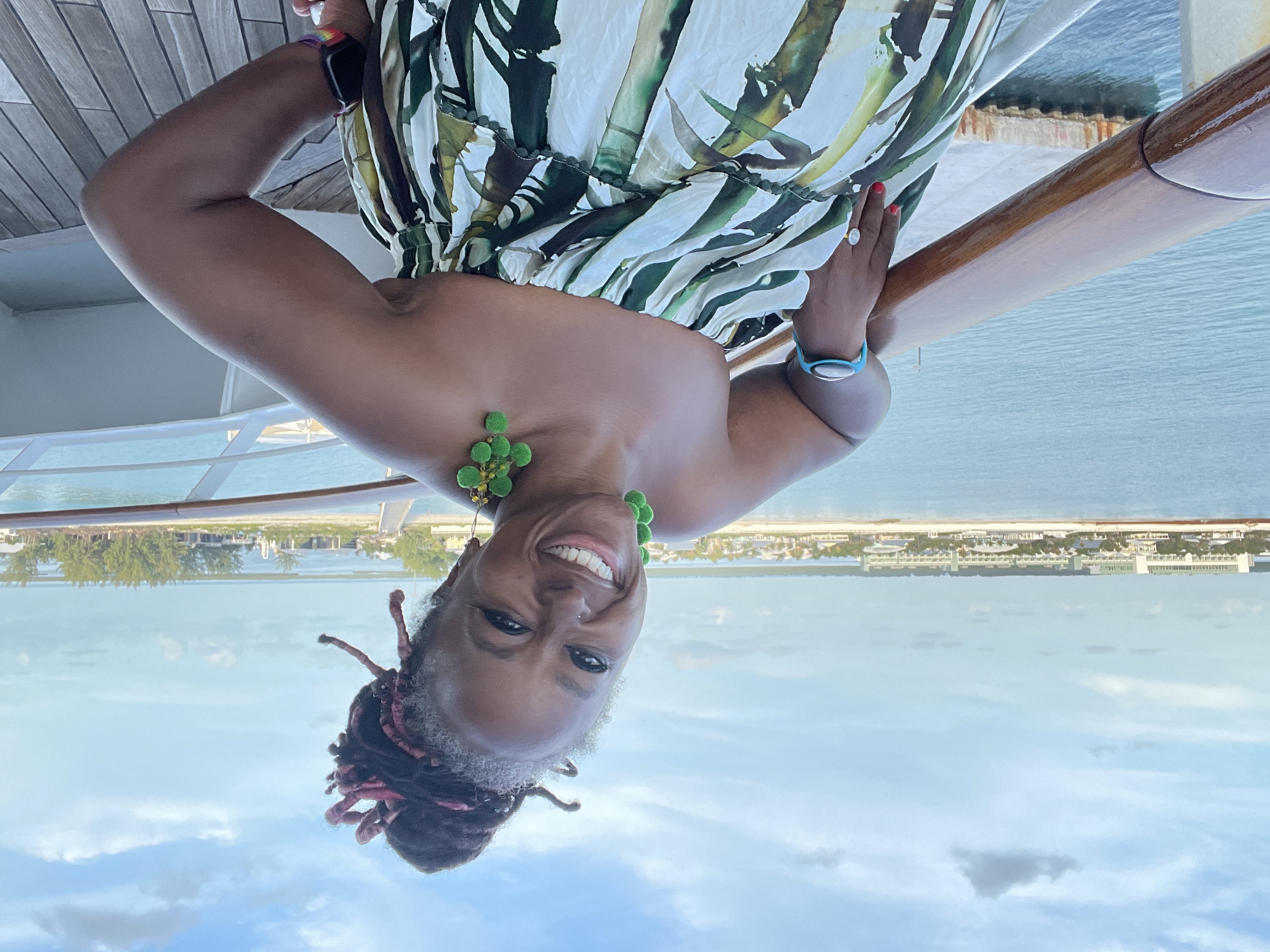 Sarah smiling at the camera on the deck of a cruise ship with water and a beach in the background